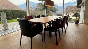 Un'area pranzo con un tavolo e sedie in legno, ampie finestre con vista sulle montagne e una pianta in vaso.