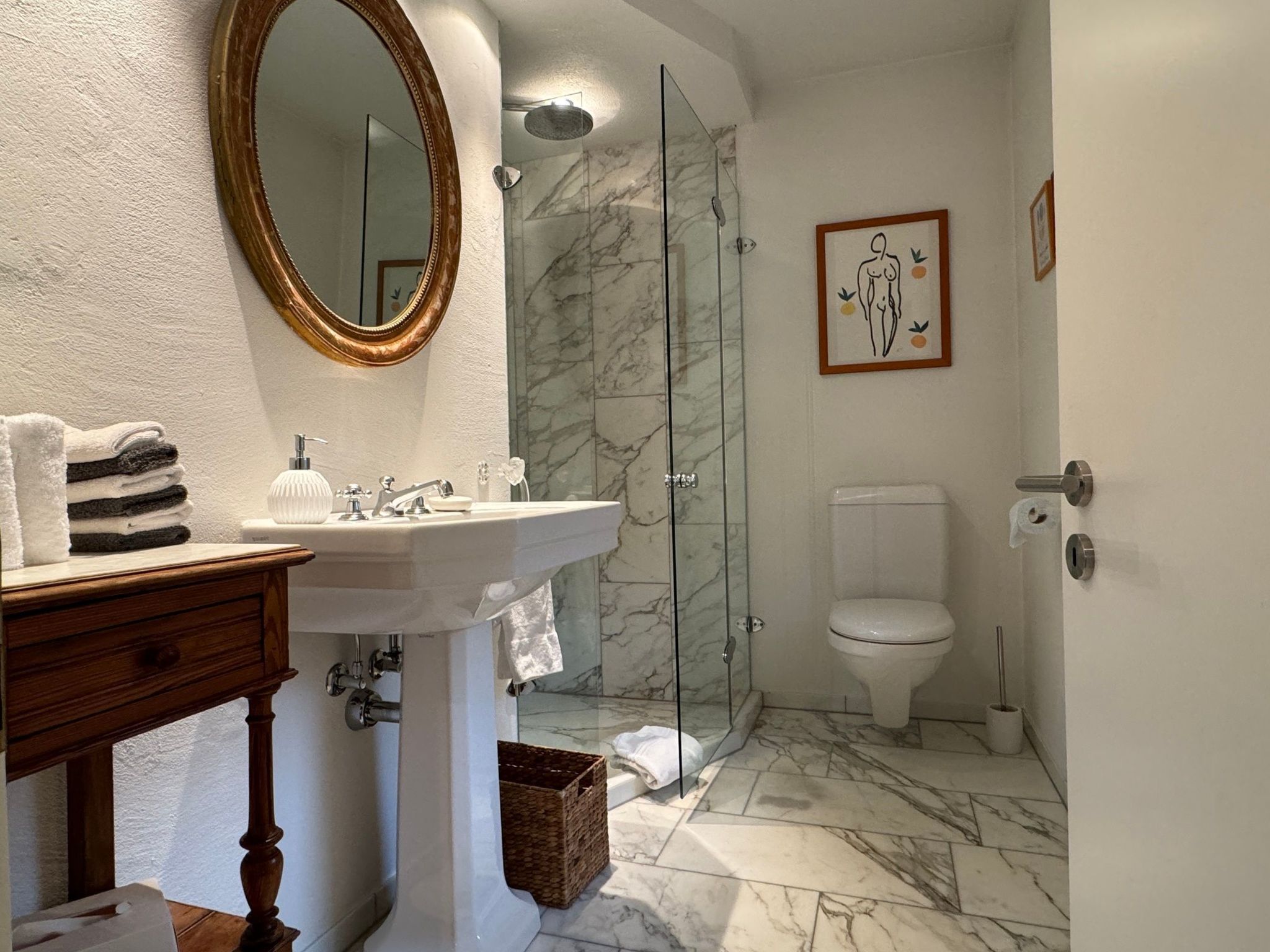 A bathroom with a marble floor, a white sink, a glass shower enclosure, and a toilet.