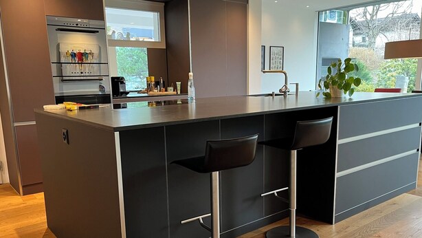 Una cucina moderna con isola centrale, sgabelli da bar e vista sull'esterno.