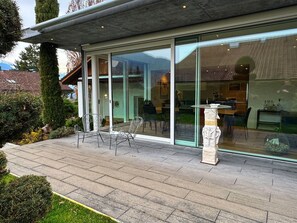 A modern house with a patio, outdoor seating, and a large glass door leading to an interior dining area.