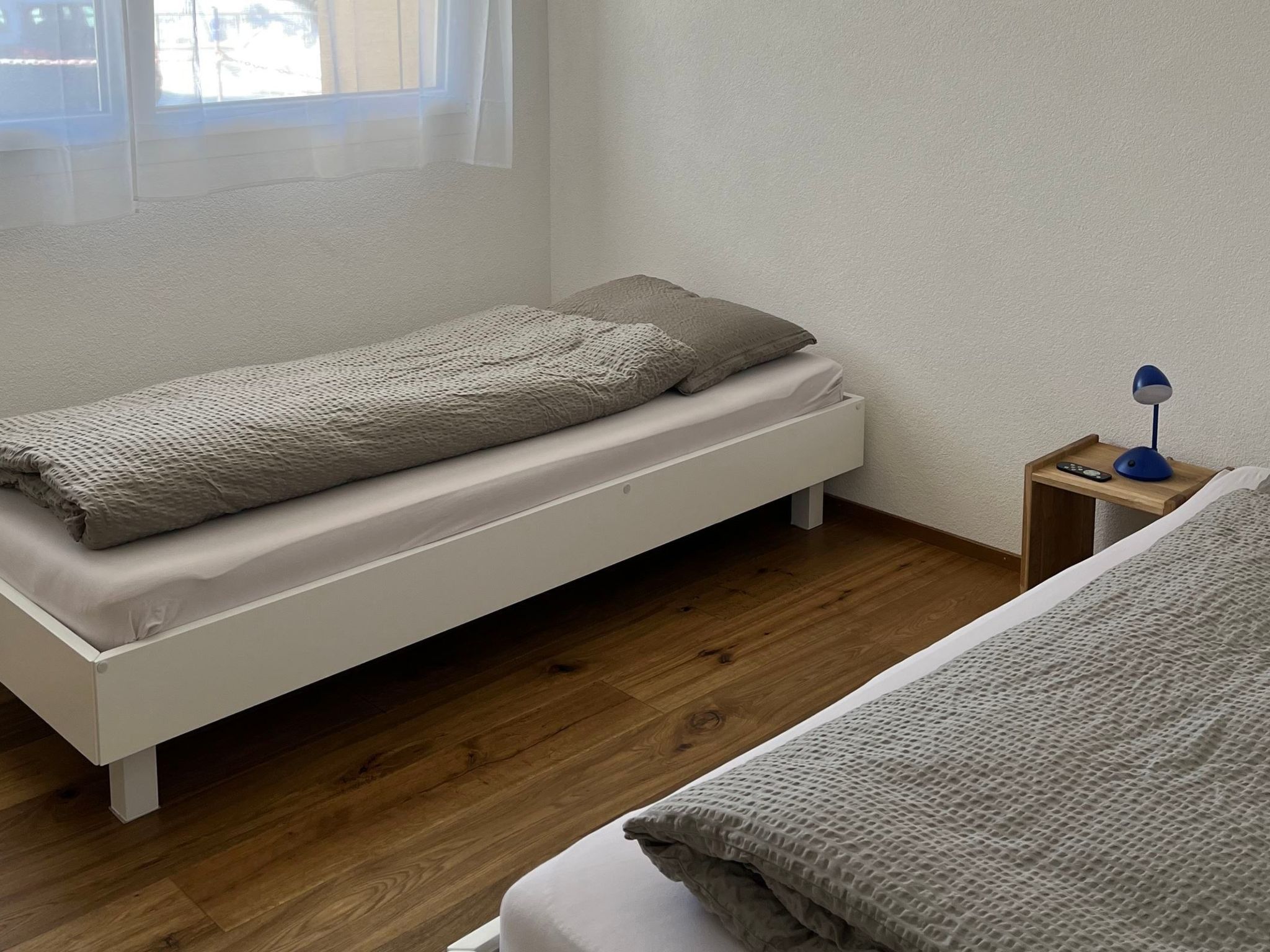 A single bed with a textured blanket and pillows, a bedside table with a lamp, and a window with curtains.