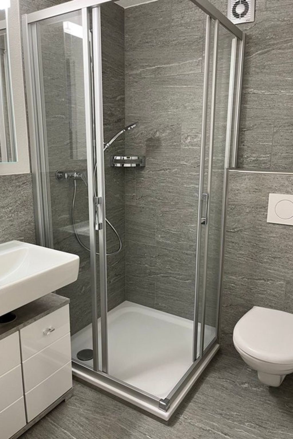 Ein modernes Badezimmer mit einer gläsernen Dusche, einem weißen Waschbecken und einer Toilette.
