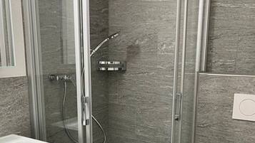 Ein modernes Badezimmer mit einer gläsernen Dusche, einem weißen Waschbecken und einer Toilette.
