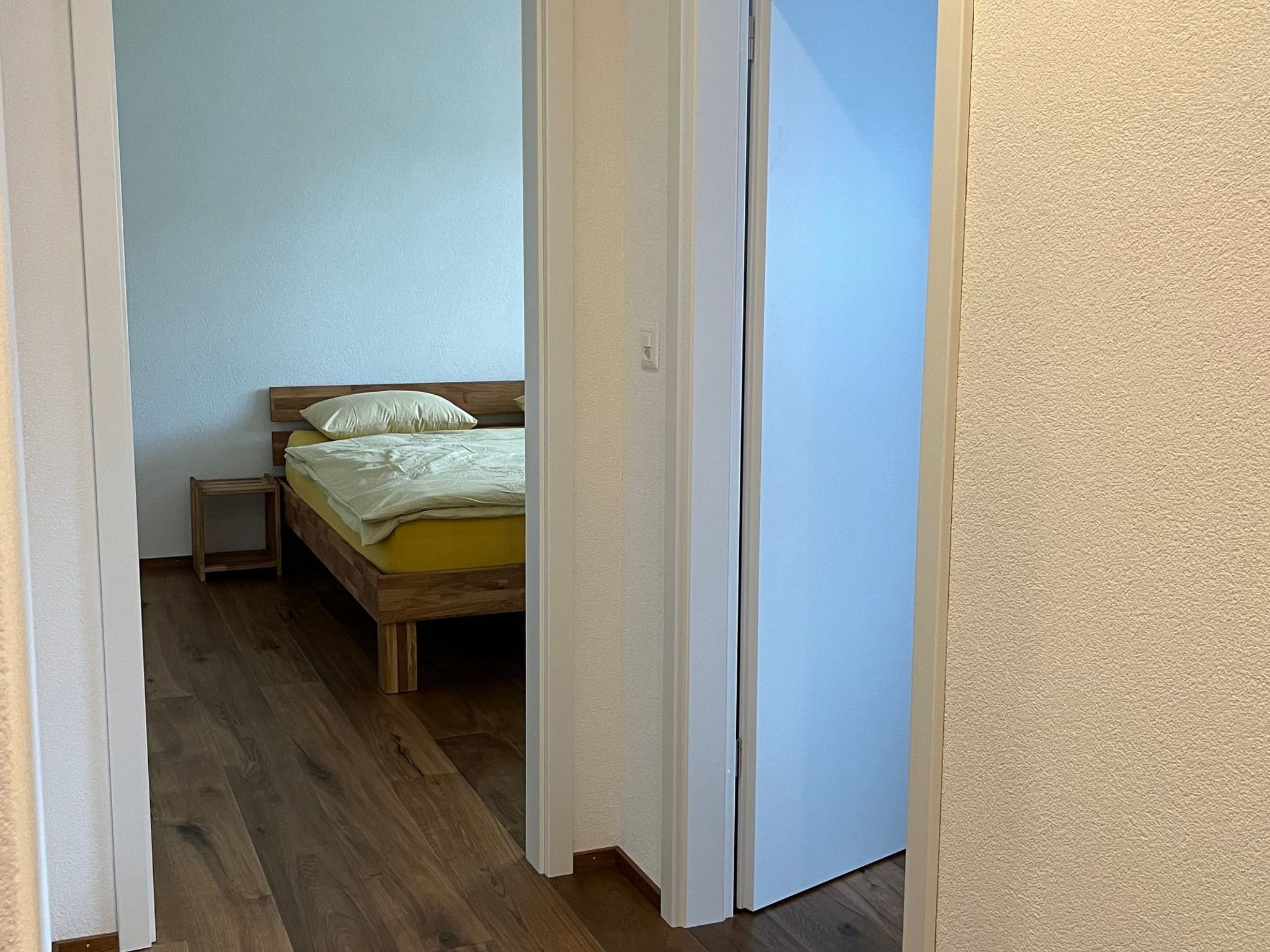 Ein Schlafzimmer mit einem hölzernen Bett, einem Nachttisch und einer Tür zu einem anderen Raum.