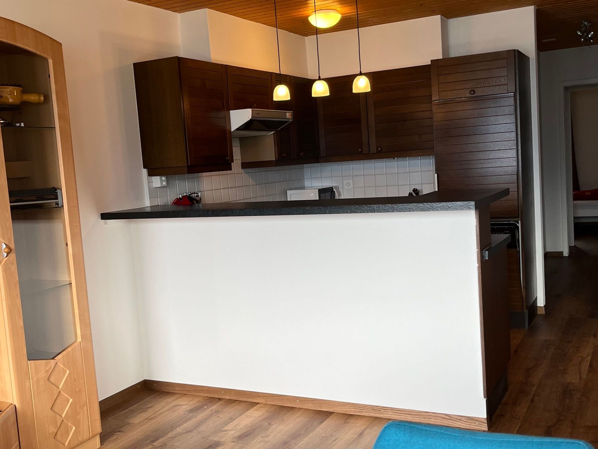 Une cuisine avec des meubles en bois, un plan de travail blanc et des luminaires suspendus.