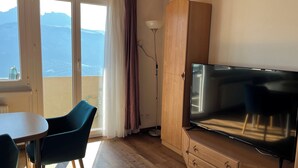 Una habitación con televisión, una mesa con sillas, un armario de madera y vistas a las montañas a través de una ventana.