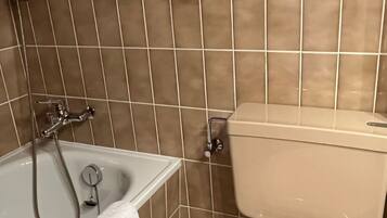 A bathroom with a bathtub, toilet, and tiled walls.