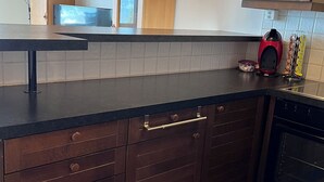Una cocina con armarios de madera oscura, encimera negra, electrodoméstico rojo y una ventana.