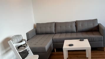 Un salon moderne avec un canapé d’angle gris, une table basse blanche et un fauteuil blanc agrémenté d’un coussin gris.