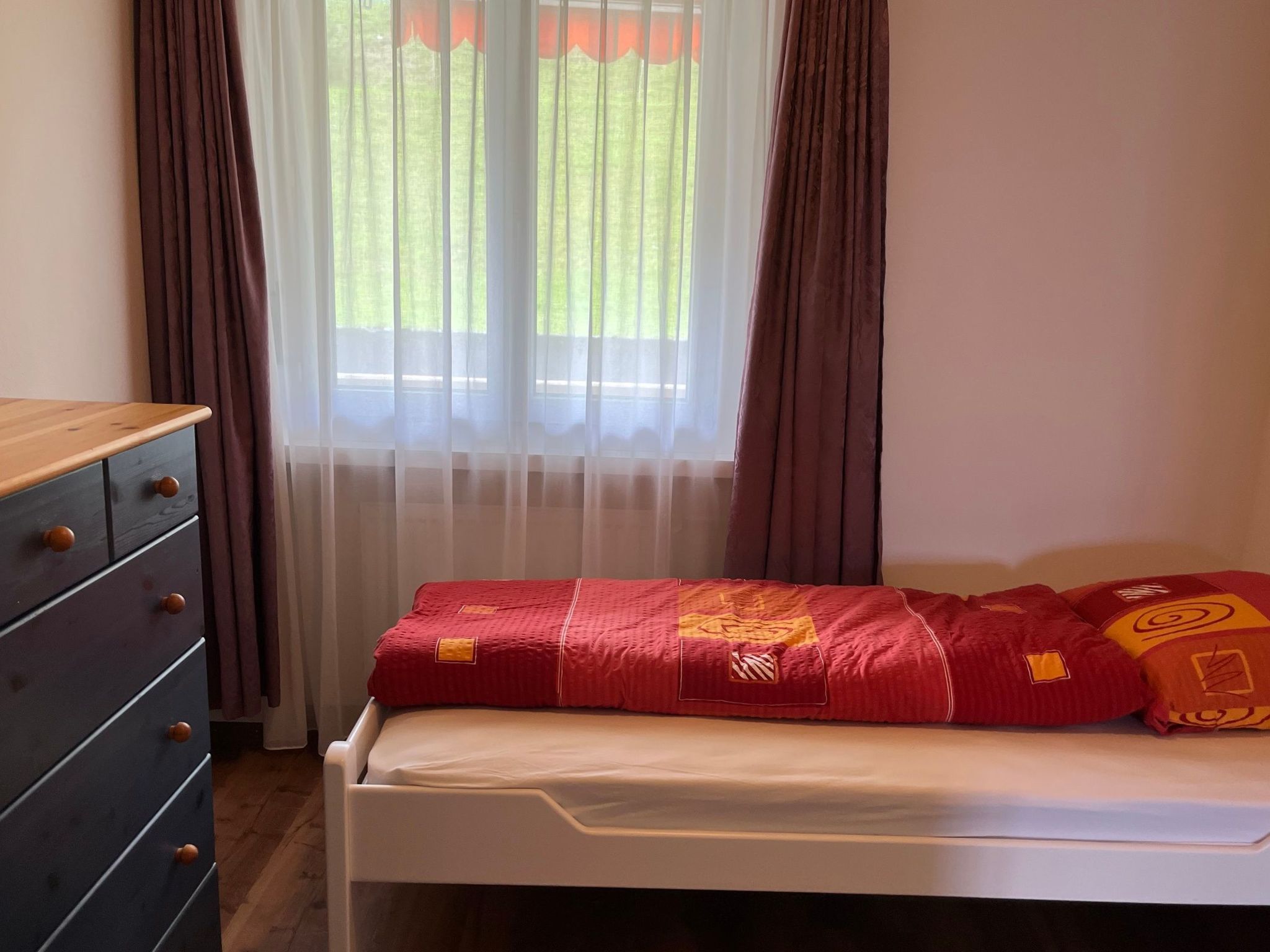 A bedroom with a bed, a dresser, and a window with curtains.