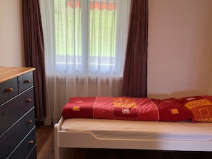 A bedroom with a bed, a dresser, and a window with curtains.