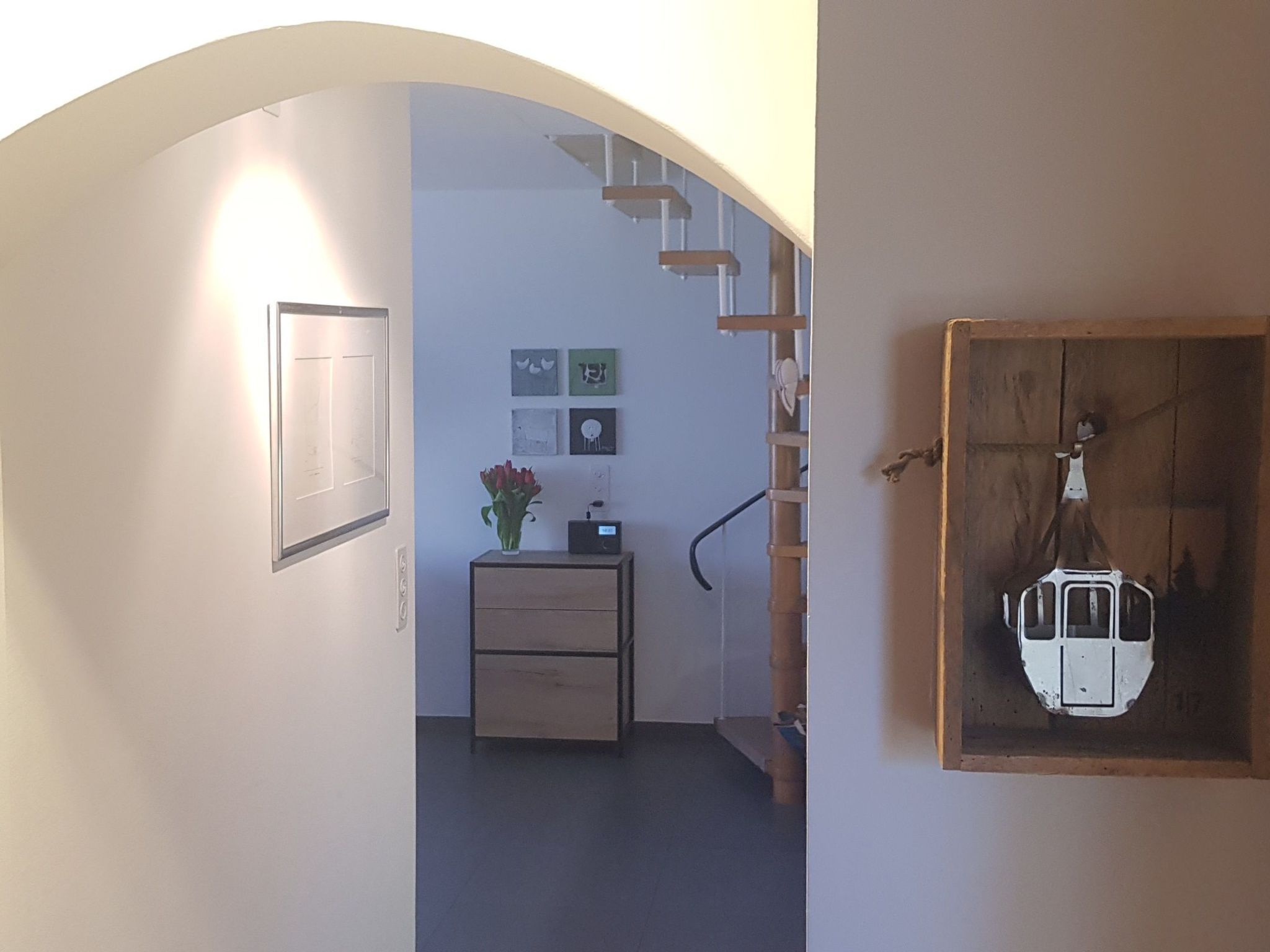 En indvendig gang med en trætrap, et lille skrivebord med en vase og billedkunst på væggen.
