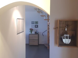 Un passadís interior amb una escala de fusta, un petit escriptori amb un ram i obra a la paret.