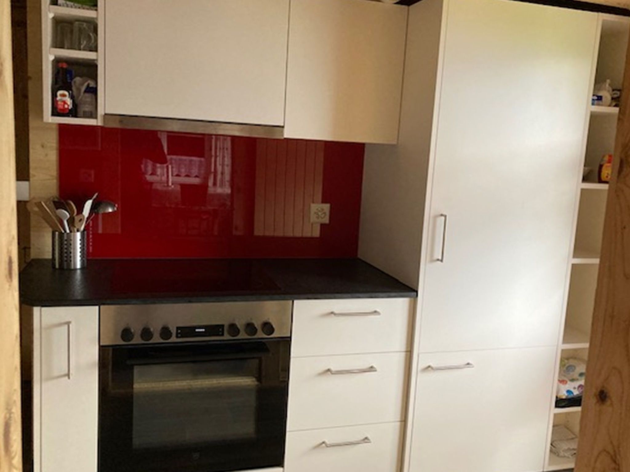Una cocina con salpicadero rojo, armarios blancos, encimera negra y horno de acero inoxidable.