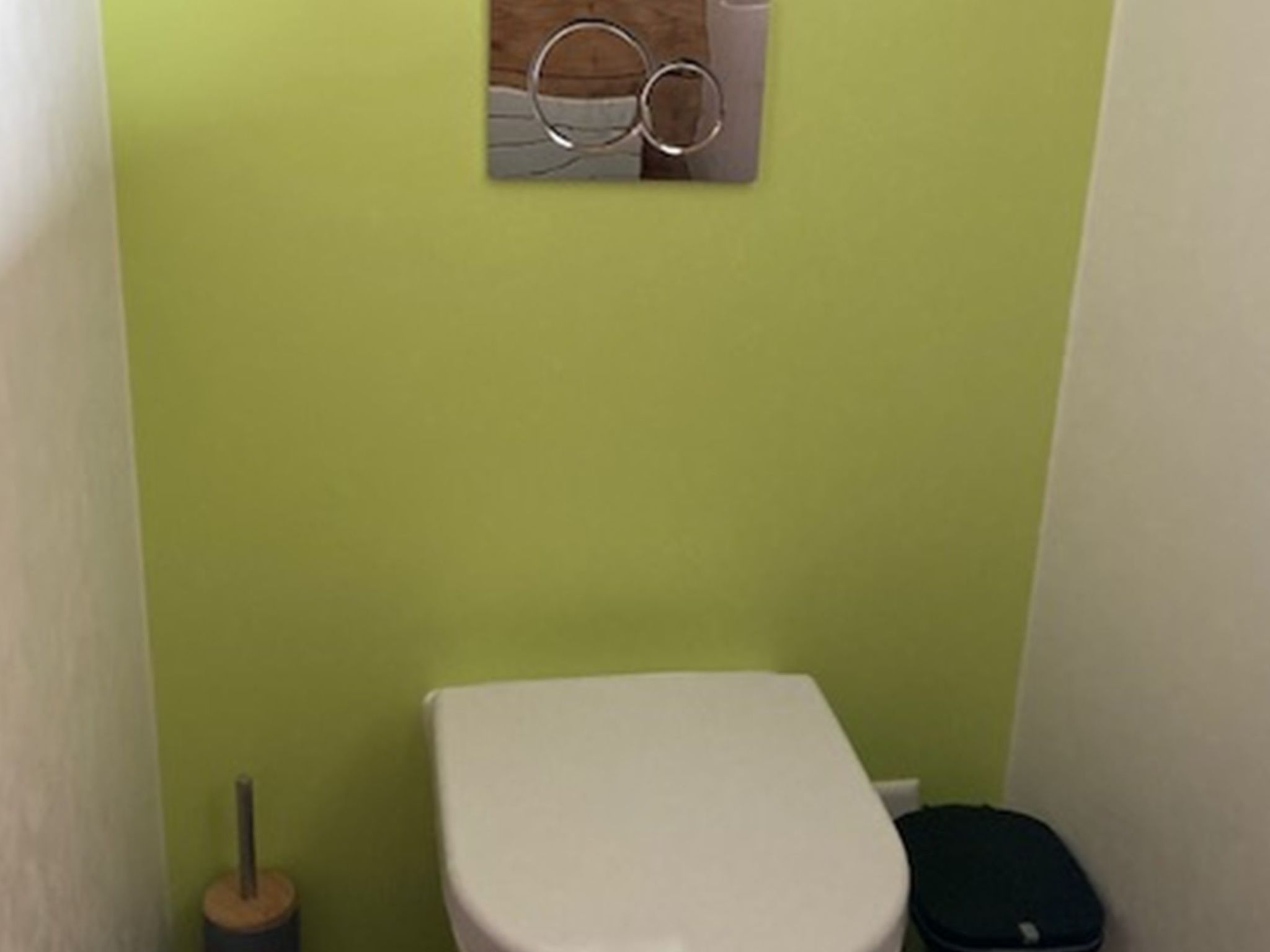 A small, narrow bathroom with a white toilet, a green wall, and a trash bin.
