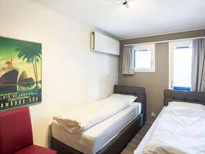 A hotel room with two single beds, a red chair, a poster on the wall, and a window with curtains. - Club Siesta Ferienwohnung/Studio, (Flumserberg Tannenheim), by Interhome (Flumserberg Tannenheim)