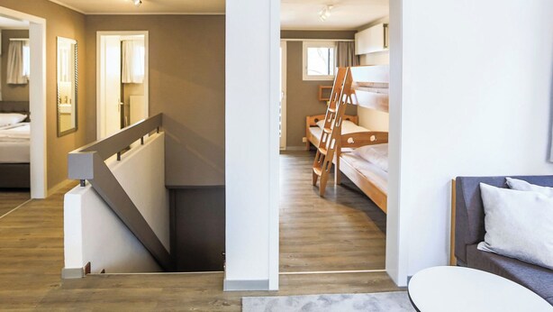 Habitación de hotel moderna con escalera, literas, sofá y un espejo grande.