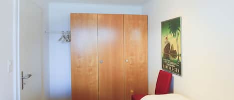 Une pièce avec une armoire, deux lits, une affiche au mur et une porte.