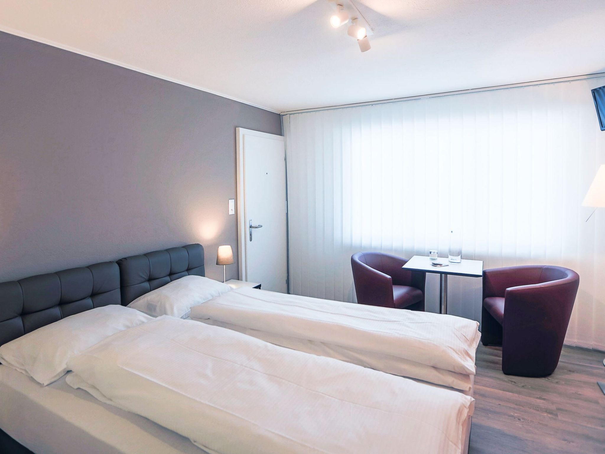 A hotel room with two beds, a desk, two chairs, and a window with curtains.