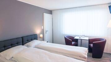 A hotel room with two beds, a desk, two chairs, and a window with curtains.