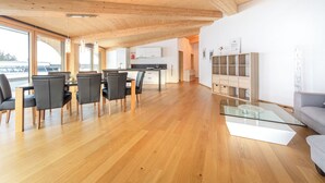 Een ruime woonruimte met houten plafond, een eettafel met stoelen, een bank en een glazen salontafel.