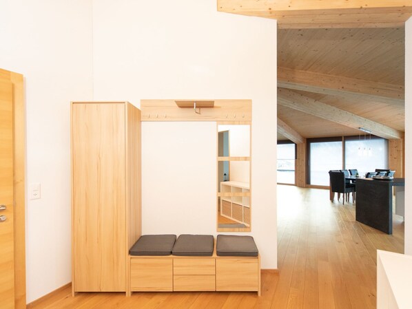 A room with a wooden wardrobe, a bench with cushions, and a desk with chairs.