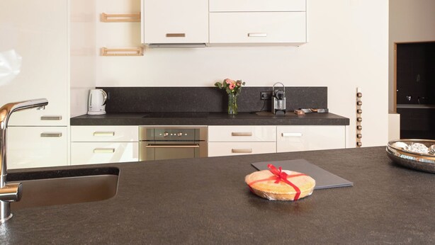 Een moderne keuken met witte kastjes, een zwart aanrechtblad en een centraal eiland met een taart.