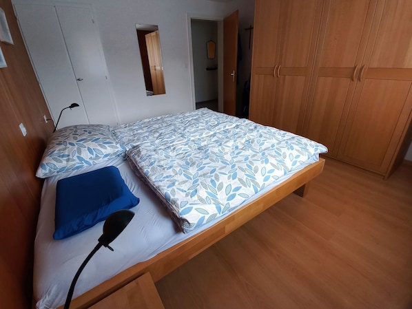 A single bed with a patterned bedspread, a blue pillow, and a bedside lamp.
