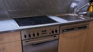 Una cocina con estufa, horno y lavavajillas de acero inoxidable, encimera de granito y armarios de madera.