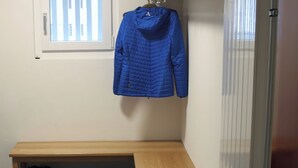 Una habitación con un banco, un perchero con una chaqueta azul y un zapatero con varios zapatos.