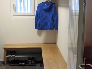 A room with a bench, a coat rack with a blue jacket, and a shoe rack with various shoes.