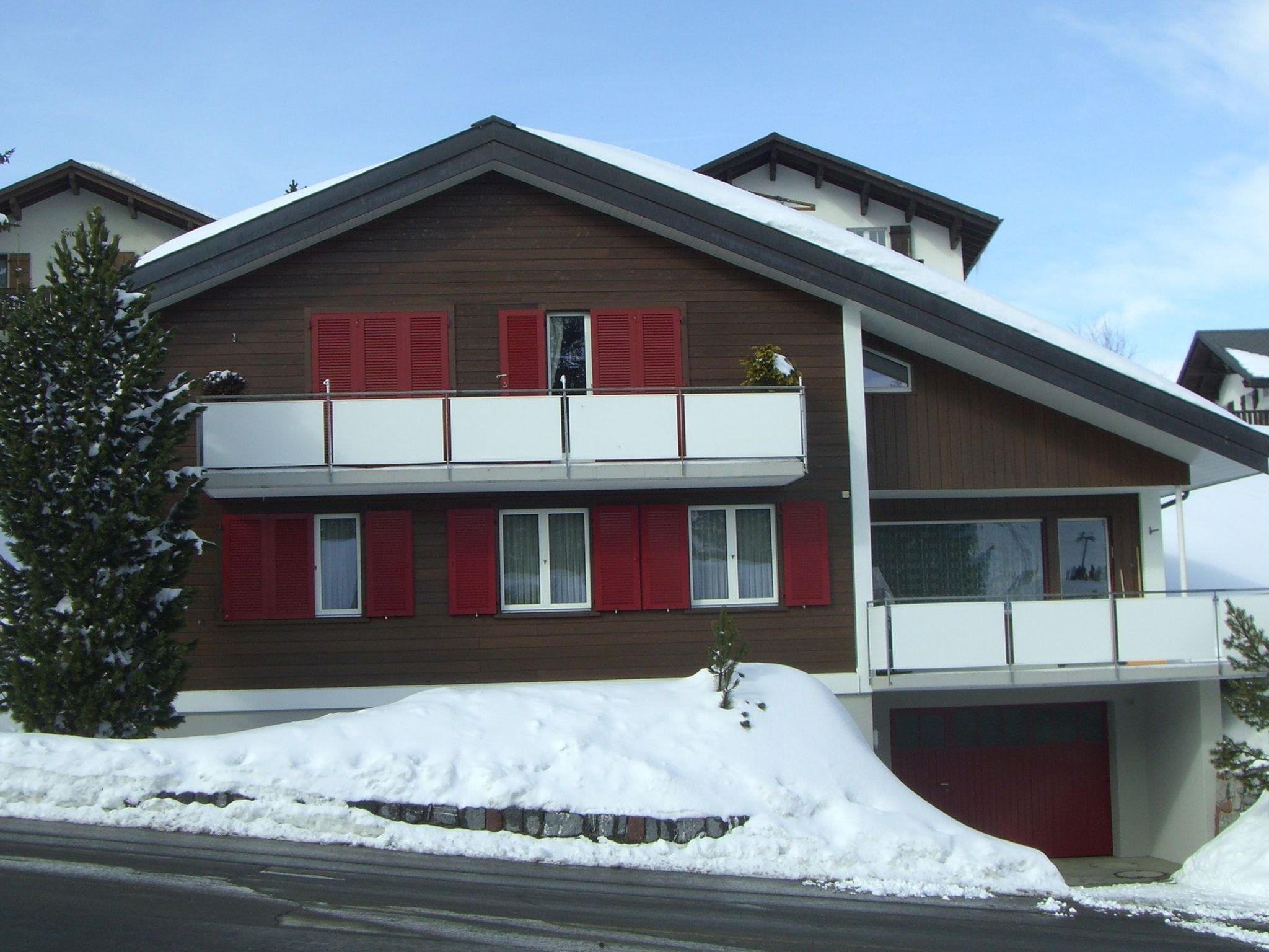 Un edificio de dos pisos con un balcón y una puerta de garaje roja.