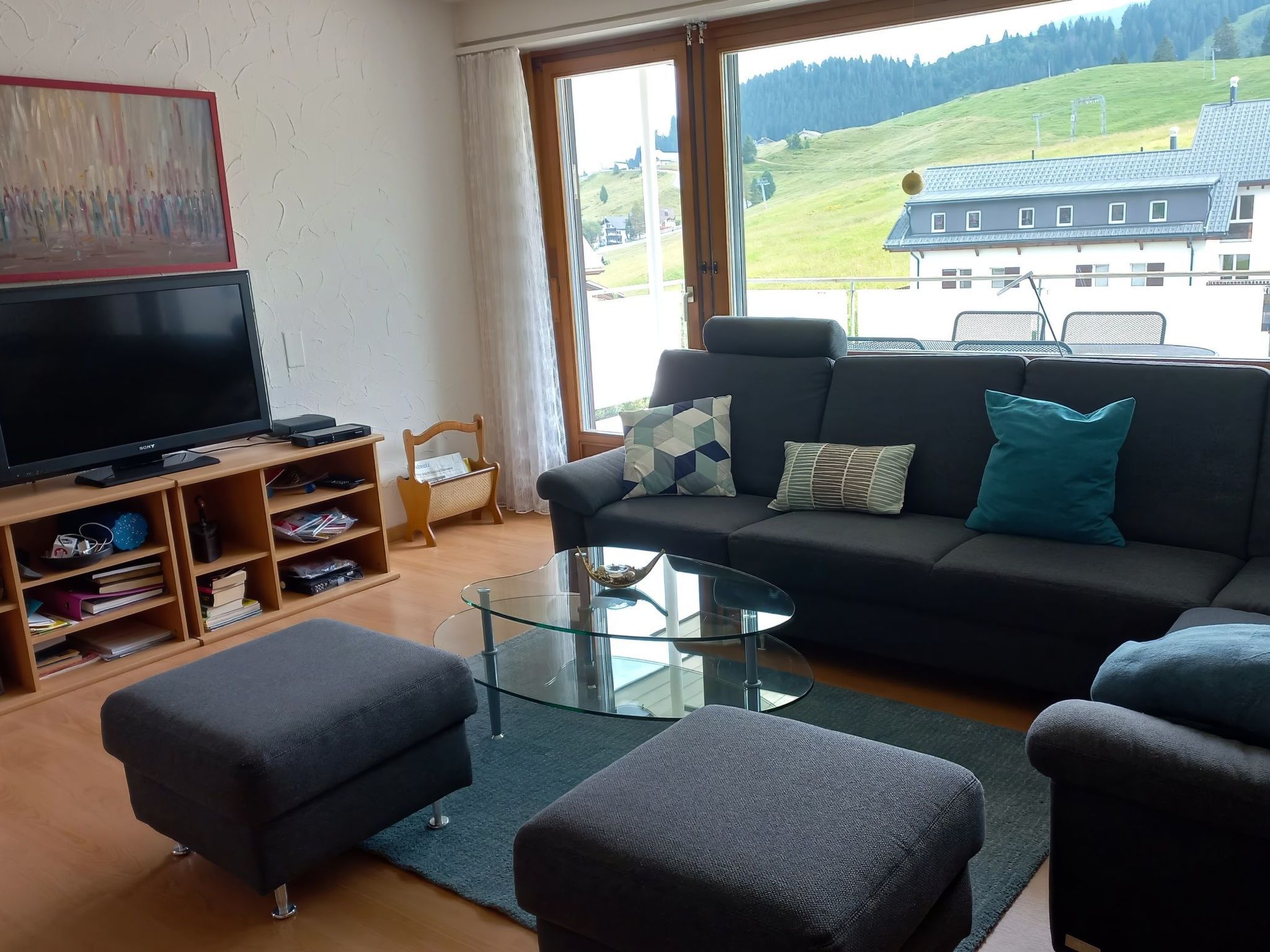 A modern living room with a sofa, ottomans, a glass coffee table, and a flat-screen TV.