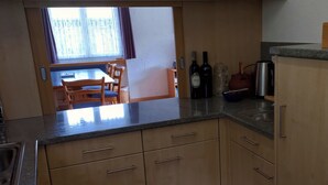 Una cocina con armarios de madera, un comedor con mesa y sillas, y un ventanal con cortinas.