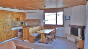 Une cuisine avec des meubles en bois, une table à manger avec des chaises, un four encastré et une cheminée.