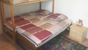 Un lit superposé avec un lit inférieur, une table de chevet, un petit tiroir et un tapis orné d’un motif représentant un paysage urbain.