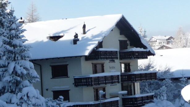 Un immeuble à plusieurs étages doté de balcons, entouré d’arbres couverts de neige.