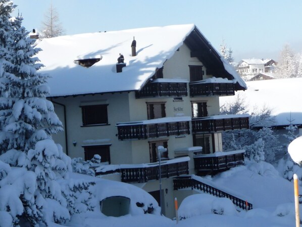 A multi-story building with balconies, surrounded by snow-covered trees.