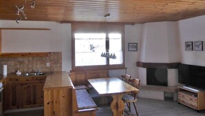 Une cuisine avec des meubles en bois, un grand îlot central, une table à manger avec des chaises, une cheminée et un téléviseur.