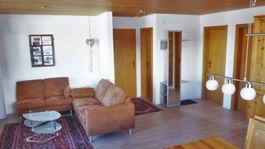 Un salon avec un canapé marron, une table basse en verre, une table à manger en bois et un tapis rouge à motifs.