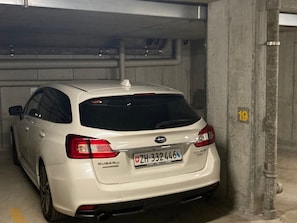 A white Subaru car parked in a concrete parking garage.