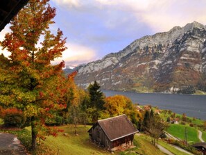 A mountain landscape with a lake, a wooden cabin, and autumn foliage.