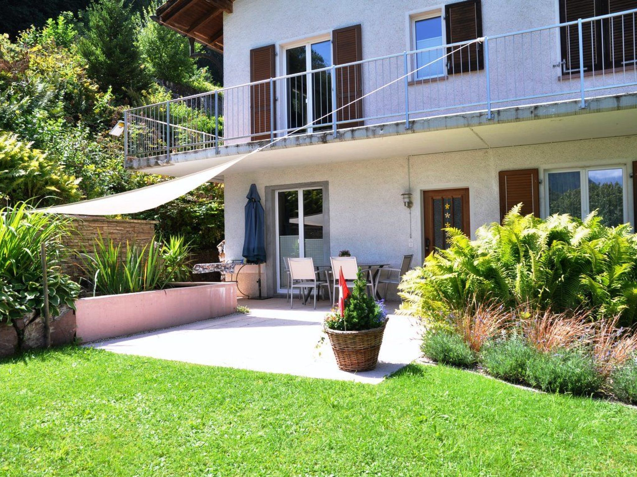 A two-story building with a balcony, outdoor seating, and a garden.