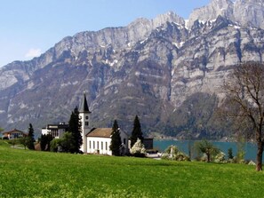 A church with a bell tower, surrounded by a grassy field and a lake, with mountains in the background. - Egglisboden, (Quarten), by Interhome (Mols)