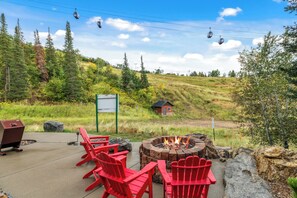 A patio with red Adirondack chairs, a fire pit, and a grill. - Storm Meadows, Ski in/out Mountain Retreat (Steamboat Springs)