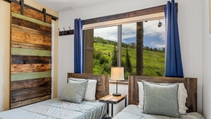 A room with two beds, a wooden headboard, a window with a view of a green landscape, and a nightstand with a lamp. - Storm Meadows, Ski in/out Mountain Retreat (Steamboat Springs)