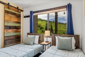 A room with two beds, a wooden headboard, a window with a view of a green landscape, and a nightstand with a lamp. - Storm Meadows, Ski in/out Mountain Retreat (Steamboat Springs)