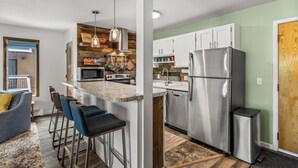 A modern kitchen with a central island, bar stools, stainless steel appliances, and a wooden accent wall. - Storm Meadows, Ski in/out Mountain Retreat (Steamboat Springs)