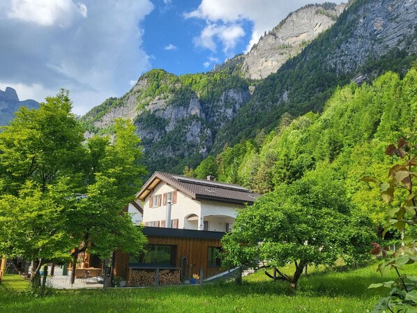 A chalet with a sloped roof, surrounded by lush greenery and mountains.