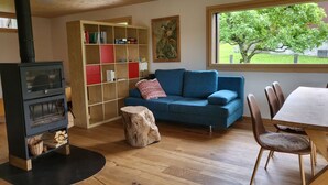 A cozy living room with a fireplace, a blue sofa, a wooden dining table, and a bookshelf. - Casa Caderas, (Berschis), by Interhome (Walenstadt)